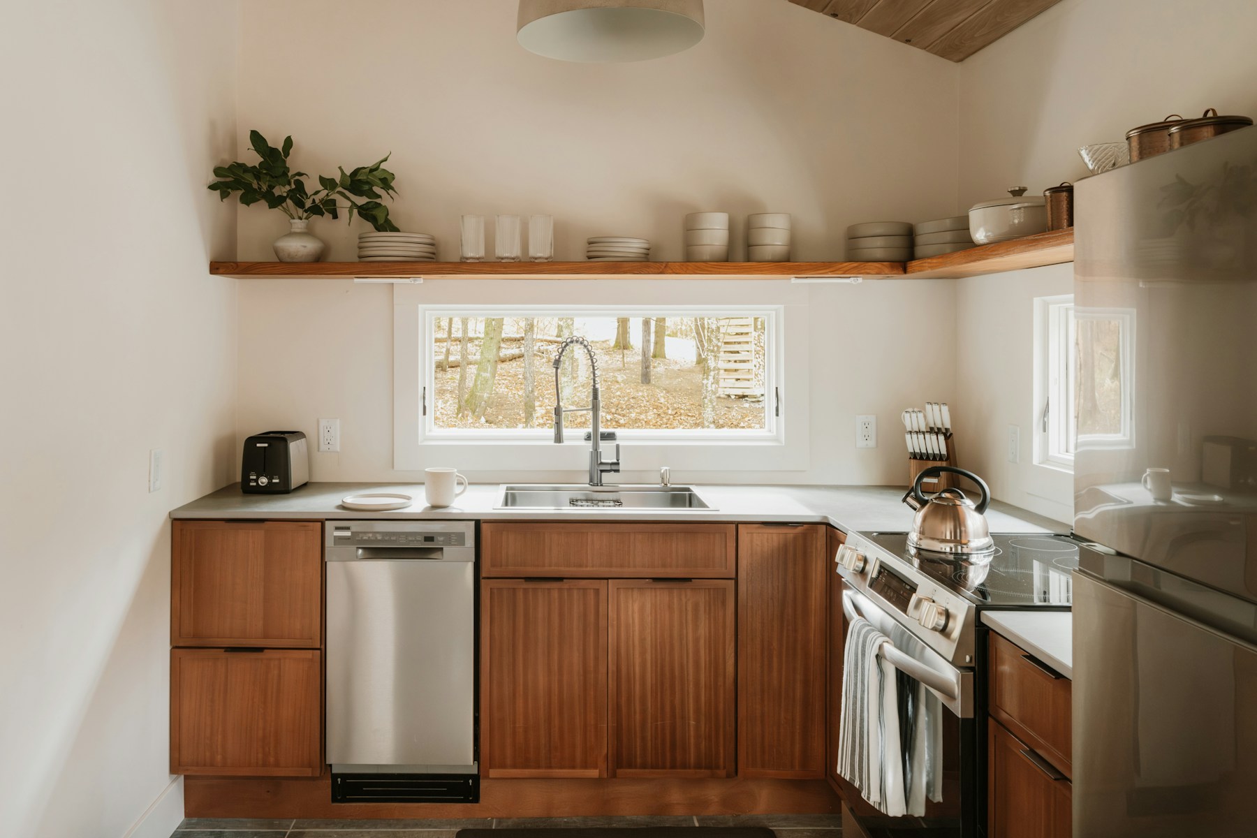 A light-filled kitchen with timber cabinetry, a stainless steel sink, and an electric range